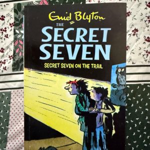 Used Book - Enid Blyton - Secret Seven on The Trail - Hachette India - In Secret Seven on the Trail, Blyton delivers a gripping masterclass in deduction. A snowy night and a mysterious message lead the team into an exhilarating railway-side chase. It is a stunning celebration of curiosity, blending cozy nostalgia with genuine tension to keep young readers hooked until the final reveal.