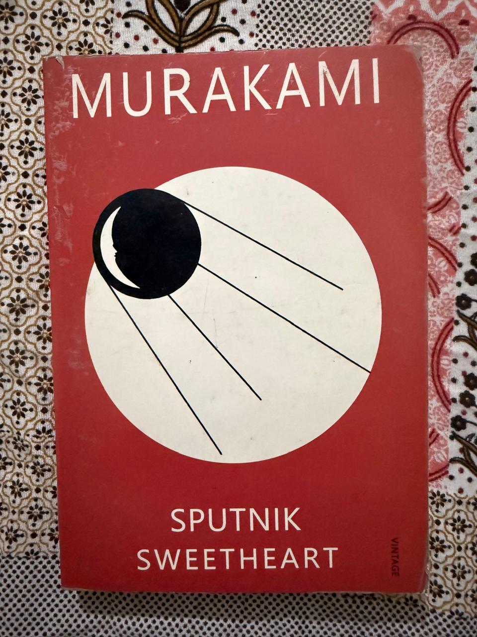 Used Book - MURAKAMI - Sputnik Sweetheart - A melancholic and dreamlike masterpiece, Sputnik Sweetheart beautifully captures the ache of unrequited love and existential loneliness. Haruki Murakami spins a mesmerizing tale of a cosmic love triangle, blurring the lines between reality and parallel worlds. It is a haunting, poetic, and deeply moving exploration of the solitary orbits of human hearts.